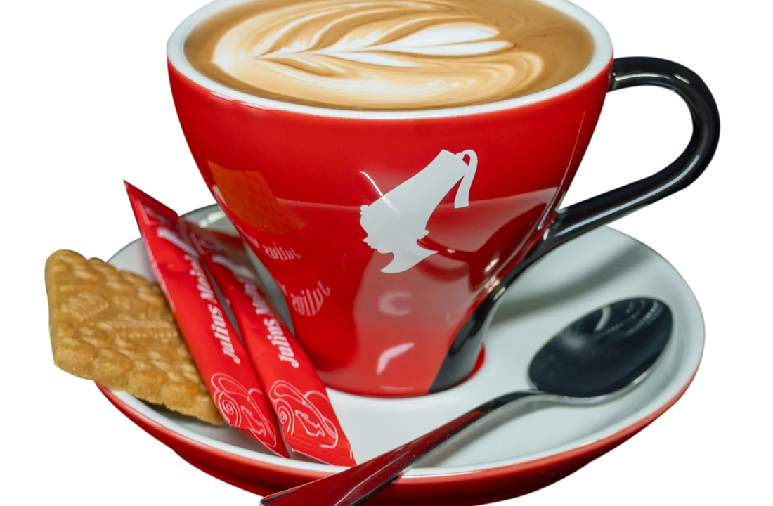 Cappuccino piros csészében, levél-mintás latte art, mellette keksszel és cukorral.